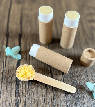 Measuring spoon containing beeswax pellets, 3 open paperboard tubes containing lip balm, and 1 paperboard lid