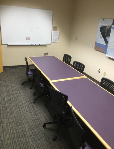 Long table with 8 chairs around and whiteboard on the wall.