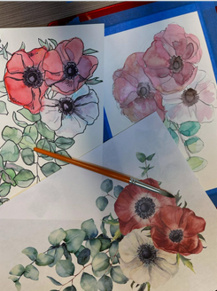 3 sheets of white paper with watercolor flowers painted on them and a paintbrush sitting on top